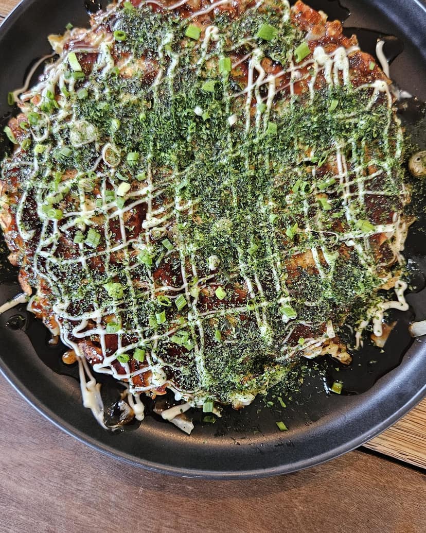 An okonomiyaki in a pan with sauce and seaweed
