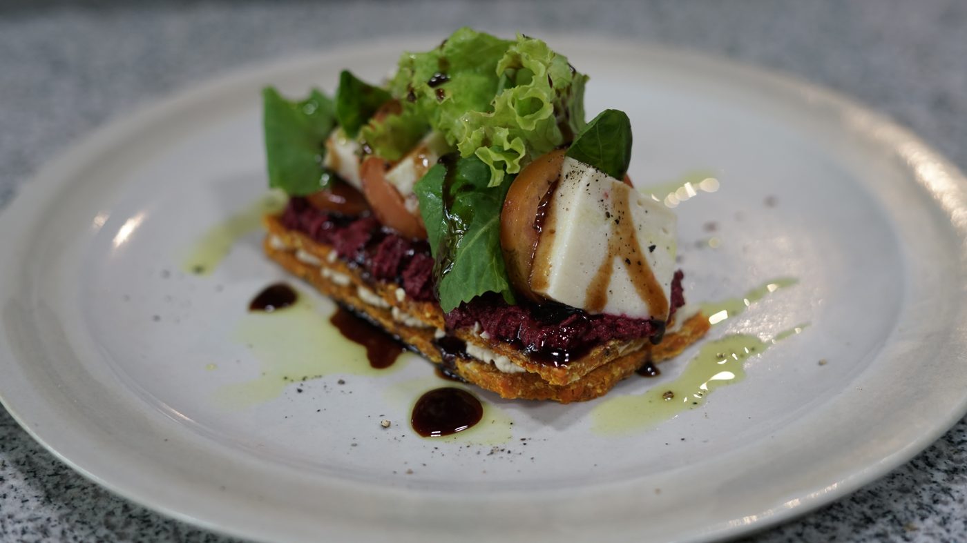 A layered beet and pastry stack with greens and balsamic