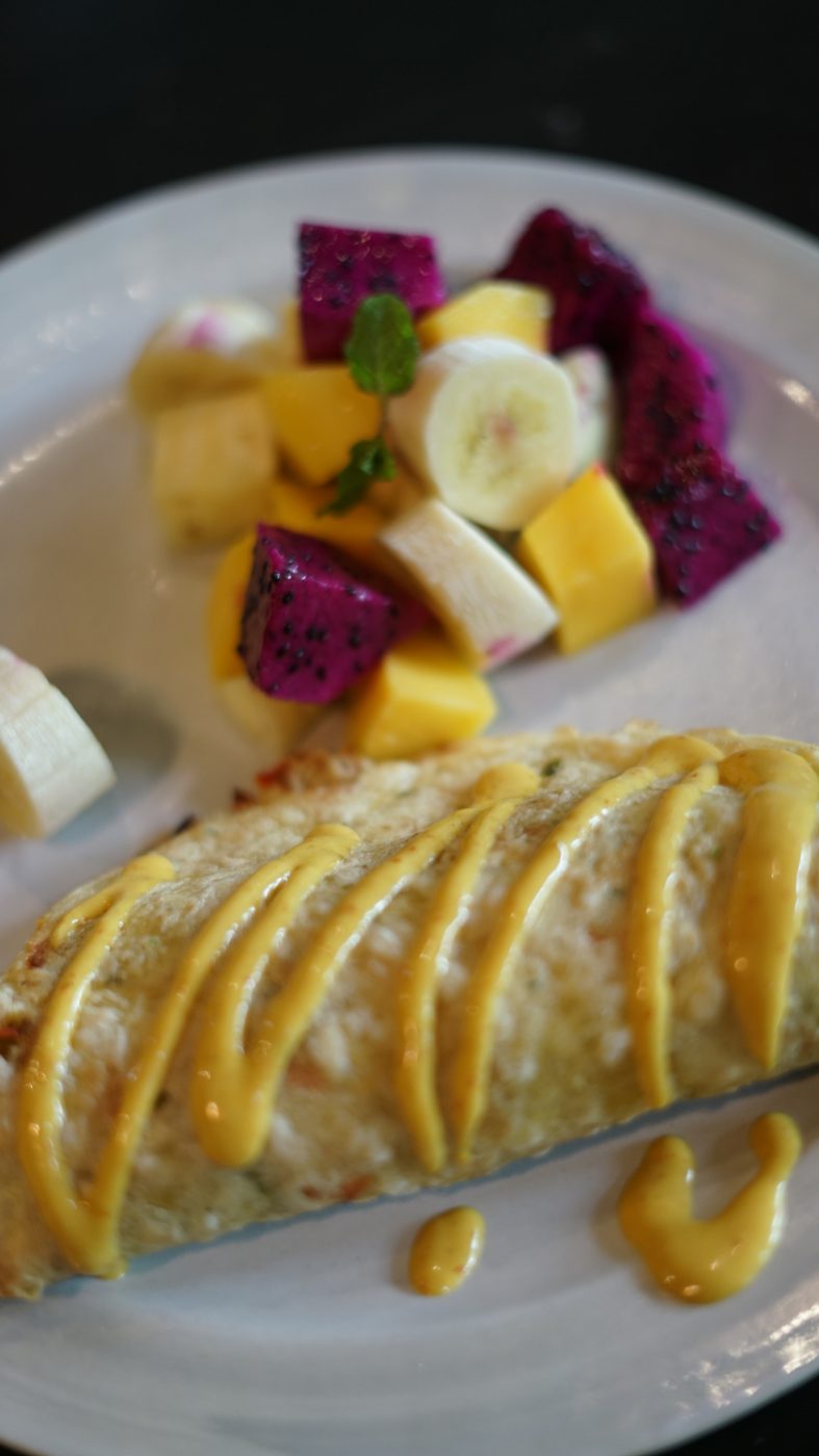 A crepe with mango sauce next to cubes of dragon fruit, mango and banana
