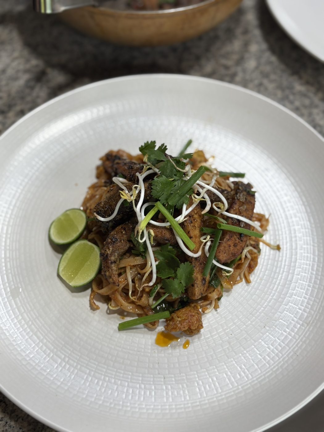 Raw pad thai with sprouts, lime and herbs on a textured plate