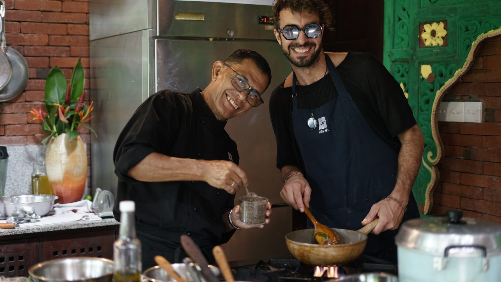 Chef Elliot and a Moksa chef laughing as they cook together at the stove