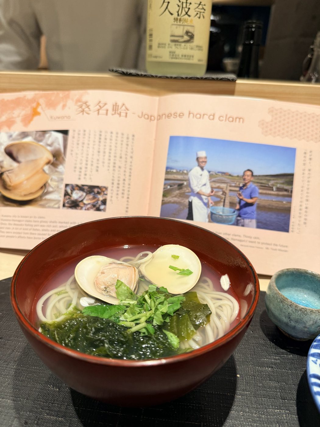 Hard-clam udon in a red lacquer bowl with wakame and herbs